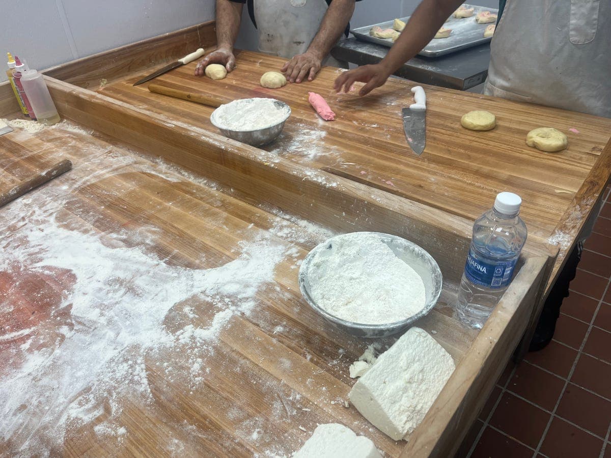 Workers shaping conchas dough with pink topping at Los Portales bakery